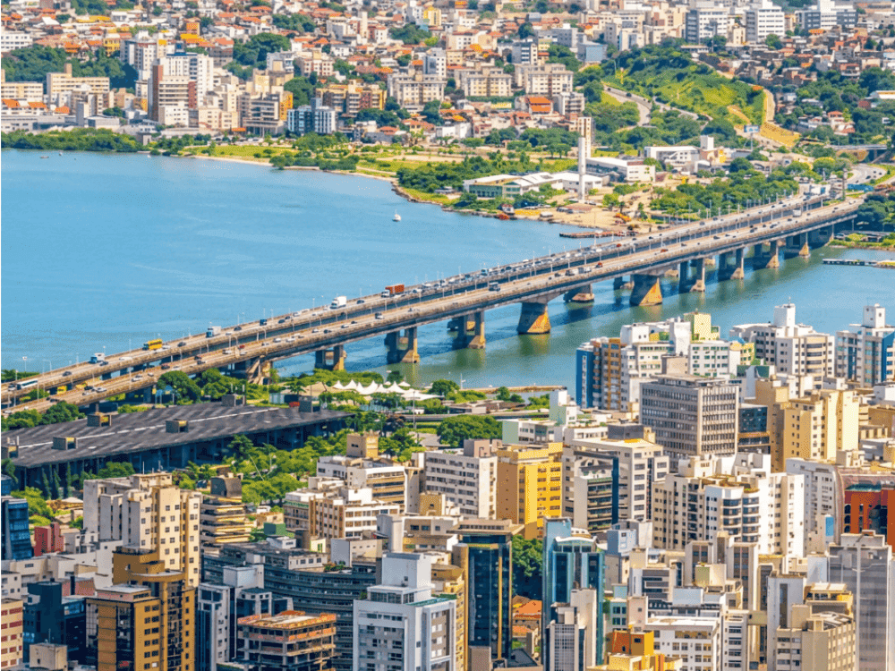 Vista panorâmica da área urbana de Florianópolis com edifícios, ponte sobre a baía e vias de acesso em destaque.