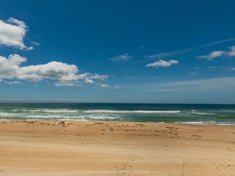 Orla extensa e tranquila no Bairro Campeche Florianópolis, com mar aberto e areia clara, ideal para esportes ao ar livre e contato com a natureza.