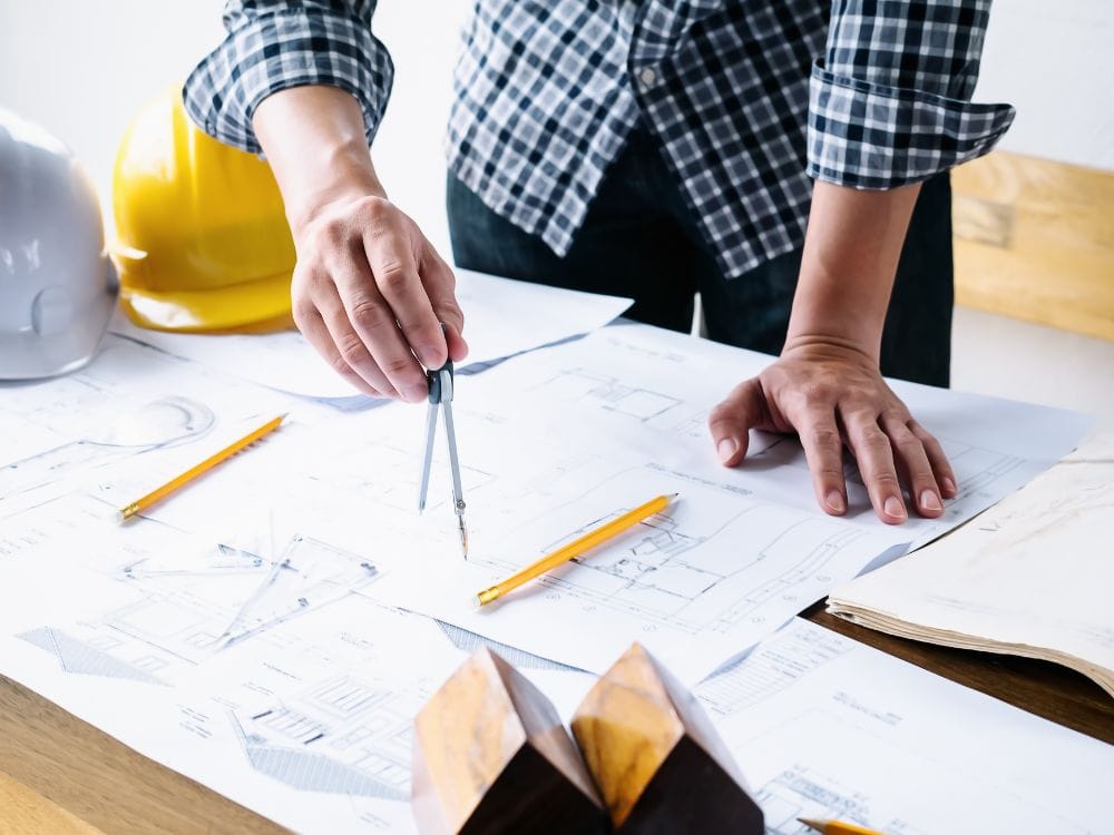 Engenheiro analisando planta arquitetônica com ferramentas de medição sobre a mesa, etapa comum no modelo BTS.