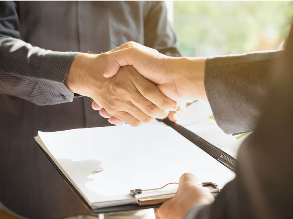 Duas pessoas apertando as mãos em sinal de acordo, com contrato em prancheta sobre a rescisão de aluguel.