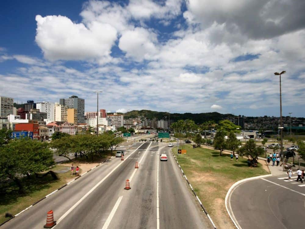 Avenida movimentada no centro de Florianópolis, com tráfego de carros, pedestres e prédios ao fundo, mostrando a vida urbana e infraestrutura da cidade. Florianópolis é seguro?