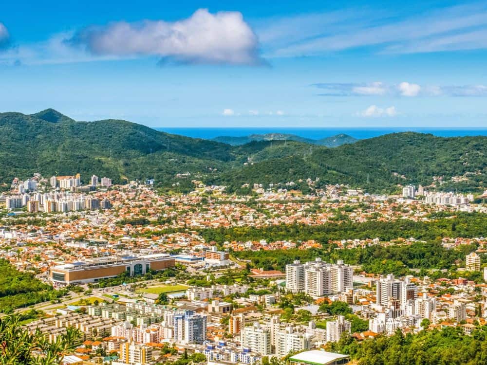 Vista panorâmica de Florianópolis, mostrando a cidade cercada de montanhas e o mar ao fundo, com a infraestrutura urbana visível. Descubra se Floripa é seguro.