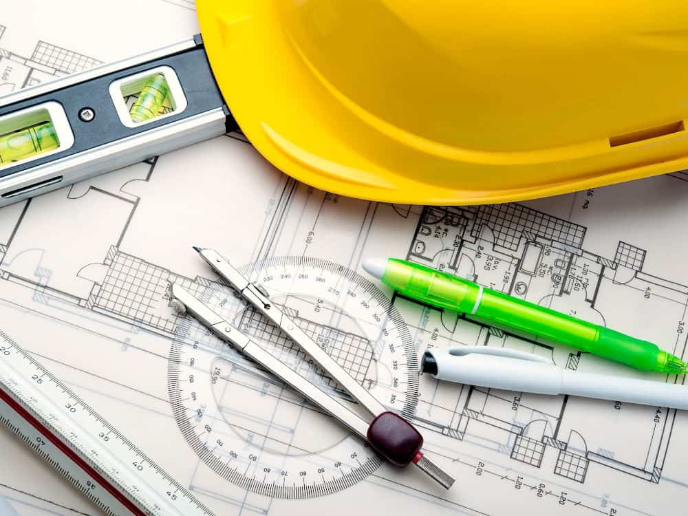 Planta arquitetônica com capacete e instrumentos de medição, representando o planejamento técnico visto em Built to Suit exemplos do mercado.