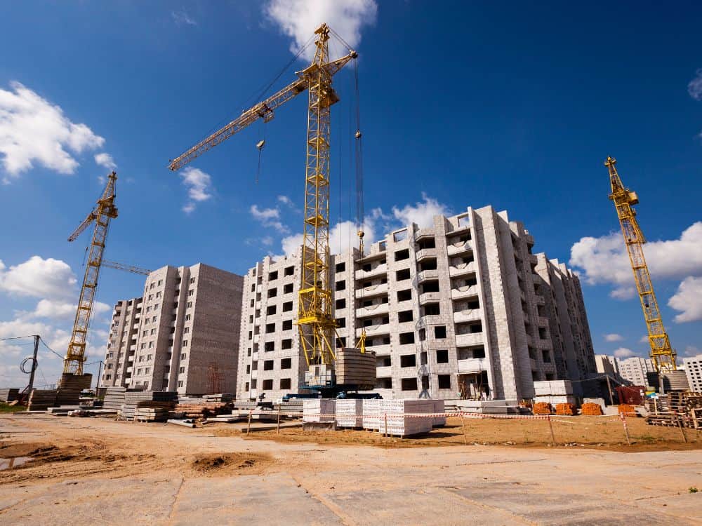 Construção de edifícios com guindastes e andaimes ilustrando o crescimento urbano e aplicação prática em Built to Suit exemplos imobiliários.