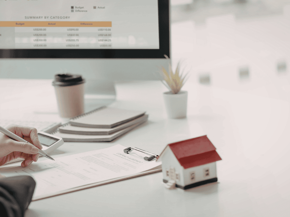 Profissional analisa documentos de financiamento com maquete de imóvel sobre a mesa, representando a avaliação para compra de imóvel usado.