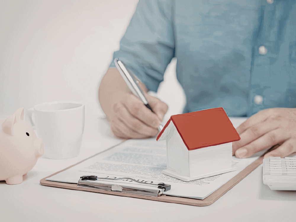 Pessoa assina documentos ao lado de uma maquete de casa, iniciando o processo de financiamento de imóvel usado com planejamento financeiro.