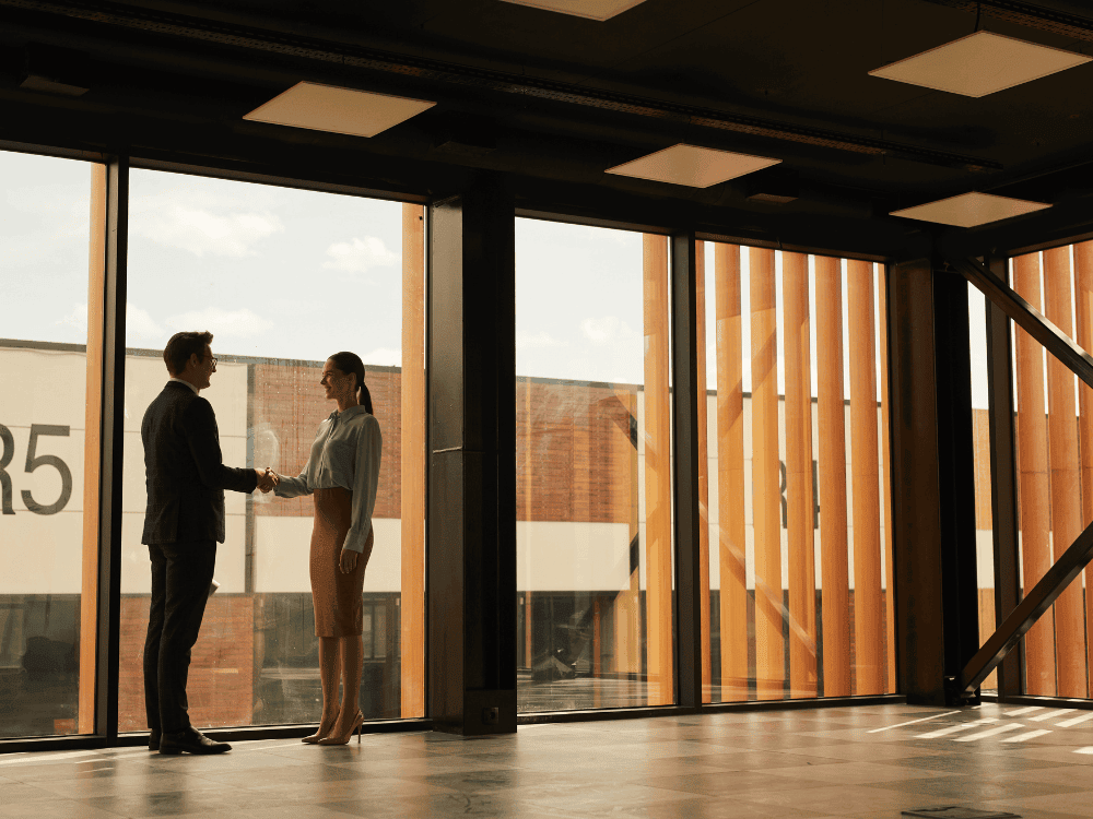 Duas pessoas apertam as mãos em ambiente corporativo, simbolizando uma negociação imobiliária baseada na valorização do imóvel.