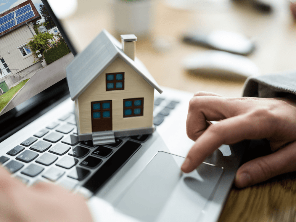 Maquete de uma casa sobre notebook com anúncio de imóvel na tela, ilustrando a pesquisa de imóveis e fatores de valorização imobiliária.