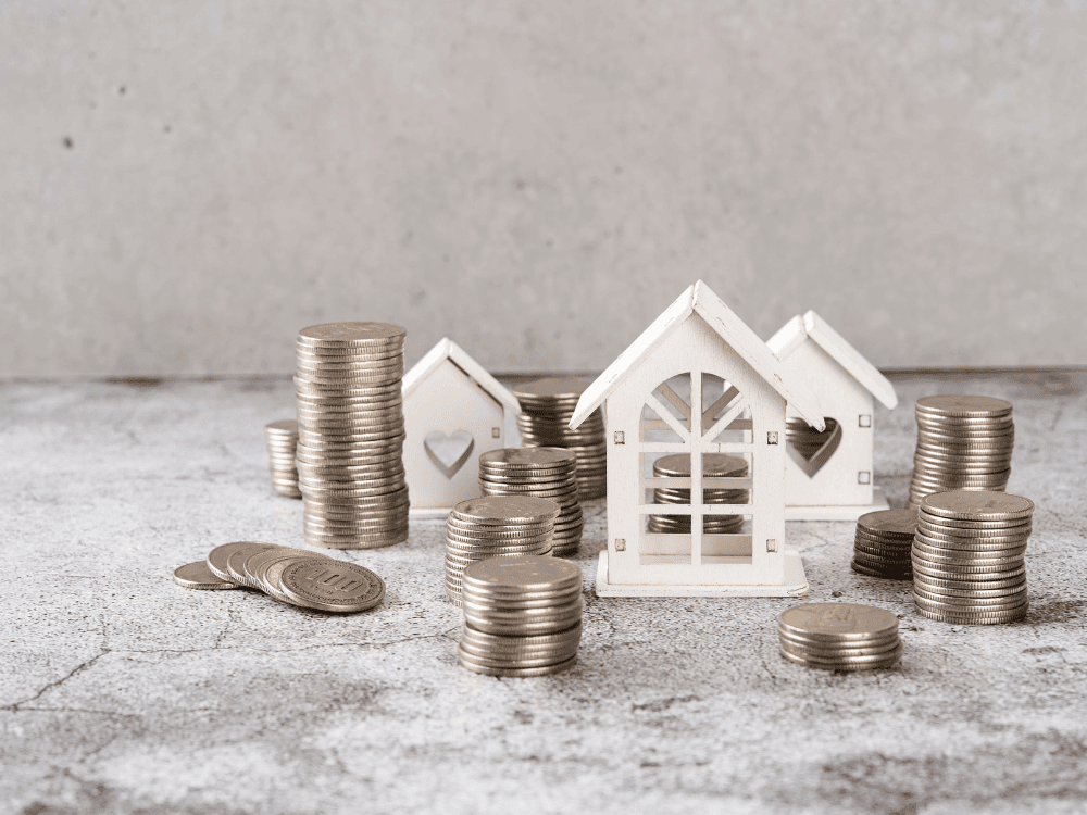 Miniaturas de casas brancas cercadas por pilhas de moedas, representando patrimônio, investimento imobiliário e potencial de rentabilidade.