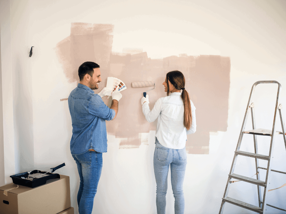 Casal pintando uma parede interna enquanto escolhe a tonalidade da tinta para renovar o ambiente antes da venda do imóvel.